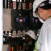 Technician wearing safety gear inspecting electrical panels in an industrial setting.