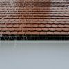 Brown roof tiles with rainwater cascading down, showcasing architectural texture and detail.