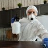 A woman in protective gear disinfecting an indoor area using a spray bottle.